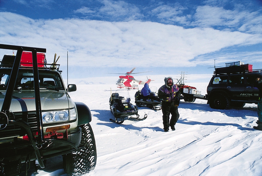 Expeditionsmedlemmar, sn&ouml;skotrar och helikopter vid tv&aring; Arctic Trucks Land Cruiser p&aring; inlandsisen.